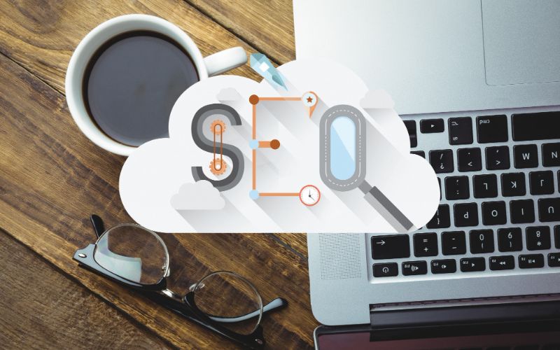 An image of a laptop and a cup of coffee placed on a cloud-shaped background, representing the concept of SEO.